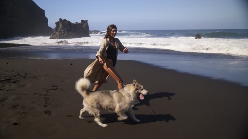 Young beautiful female model running on the beach with her husky dog. Black sand, 4K