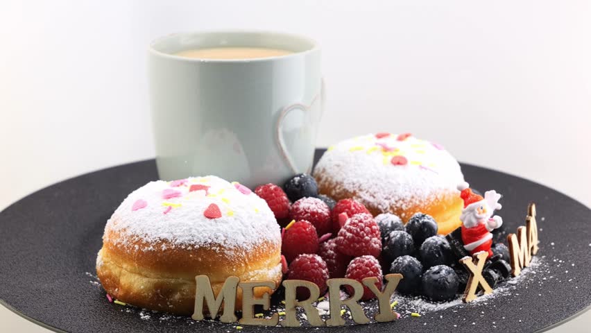 The inscription Merry Xmas (Christmas) in English. Wood letters, a cup of cappuccino, doughnuts with icing sugar, berries (raspberries, blueberries) rotating on a plate.  | Shutterstock HD Video #1112025591