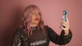 Valentine day. White happy pink hair woman wear glitter dress using mobile phone, recording video for blog while laughing isolated over pink background. 
