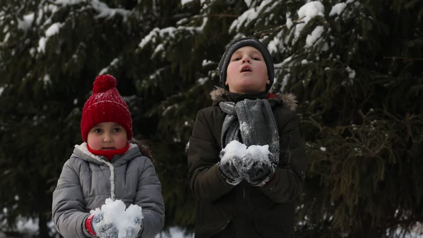 Happy kids girl and boy playing outdoor in snowy winter forest and throwing snow. Active winter holidays celebrate concept. Happy childhood