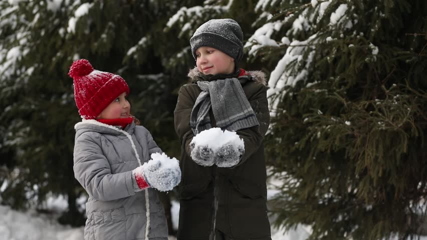 Happy kids girl and boy playing outdoor in snowy winter forest and throwing snow. Active winter holidays celebrate concept. Happy childhood