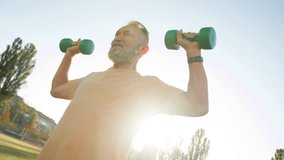 Old Caucasian man exercising with dumbbells muscle sport city stadium outside physical activity training motivation vitality pensioner gymnastic workout morning strong fitness healthcare weight energy - Powered by Shutterstock - Get 15% off with code: PIKWIZARD15