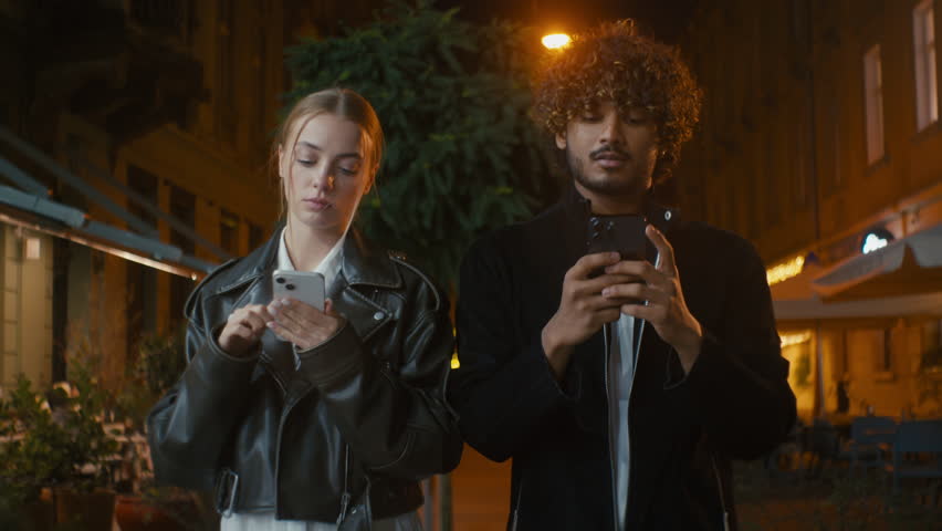 Couple walking city outside street night European woman and Indian Latino Arabian man texting using smartphone mobile phone multiracial disorder problem frustrated offended girl ignore guy separation | Shutterstock HD Video #1112037509