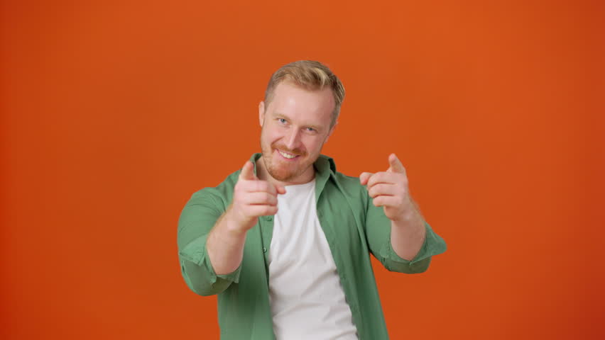 Energetic man dances with moving arms walking around studio with orange background. Male instructor showing good attitude and movements for students of art class