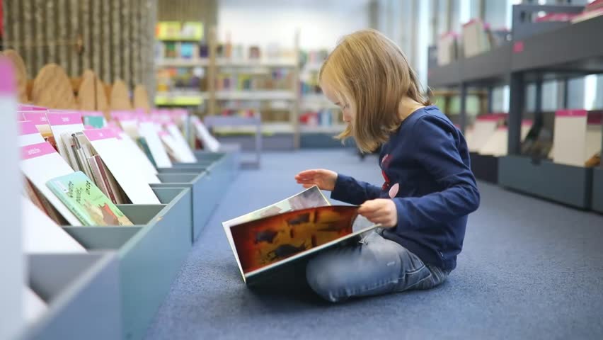 Adorable preschooler girl sitting on the floor in municipal library and reading book Royalty-Free Stock Footage #1112042947