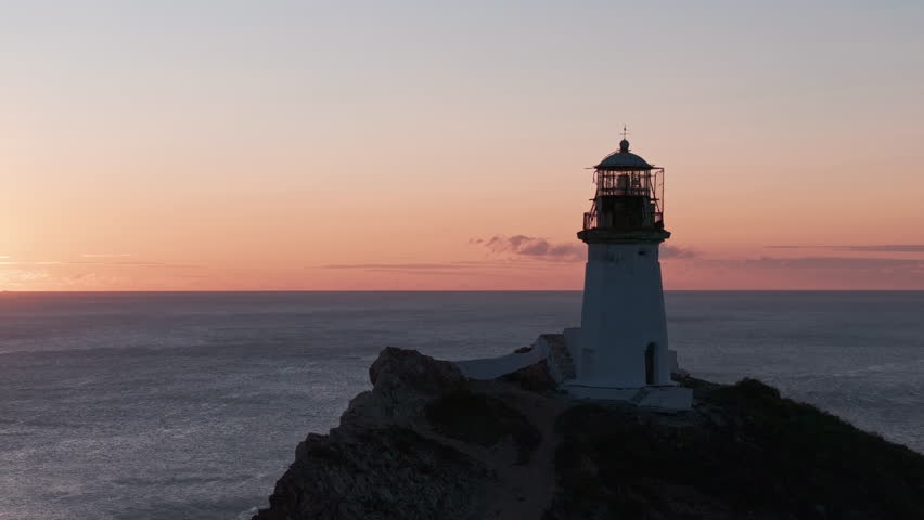 Sunset Glow Behind Majestic Lighthouse on Serene Rocky Outcropping