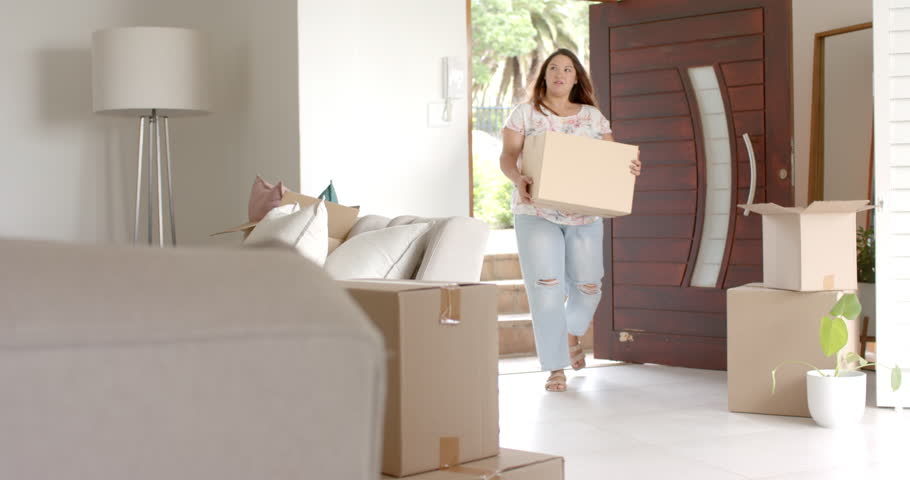 Happy plus size biracial woman carrying box, moving into new home, copy space, slow motion. Property, moving house, new home, home ownership, domestic life and lifestyle, unaltered.