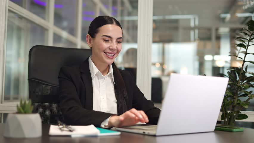 Happy woman entrepreneur sitting at table and closing digital laptop while smiling in office. Optimistic freelancer leaning on chair and rejoicing at successful completion of deadline in room. | Shutterstock HD Video #1112053071