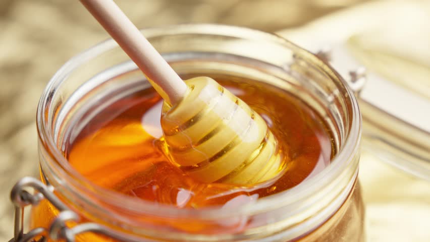 Honey dripping. Dipping honey with honey scoop in glass jar. Healthy organic food. Thick honey dripping from wooden spoon. Close-up in 4K, UHD | Shutterstock HD Video #1112055653