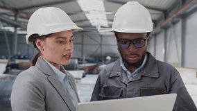Two multiethnic workers analysing products of manufacture on laptop. Young woman talking with handsome foreman while standing in workshop. Teamworking. Coworkers helping each other. Business concept - Powered by Shutterstock - Get 15% off with code: PIKWIZARD15