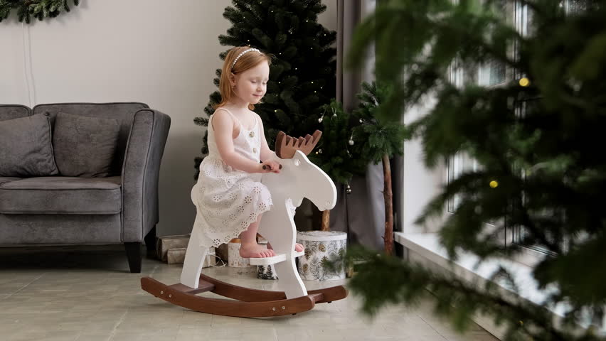 Little girl swinging on rocking horse at Christmas morning. Little child sway on wooden rocking horse near bright window. Christmas and new year celebration concept. 4K, UHD | Shutterstock HD Video #1112057349