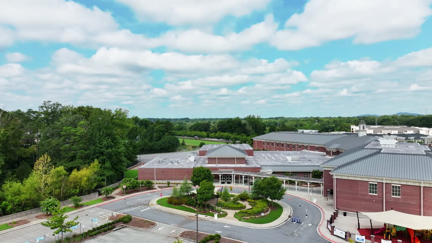 Aerial ascending footage of school complex with sports facilities. Residential suburb in flat landscape with lot of trees. Atlanta, Georgia, USA
