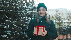 Happy young attractive woman with xmas gift box in hands on Christmas market. Cheerful beautiful girl hold shopping present box in hands. Winter holidays sale. High quality FullHD footage