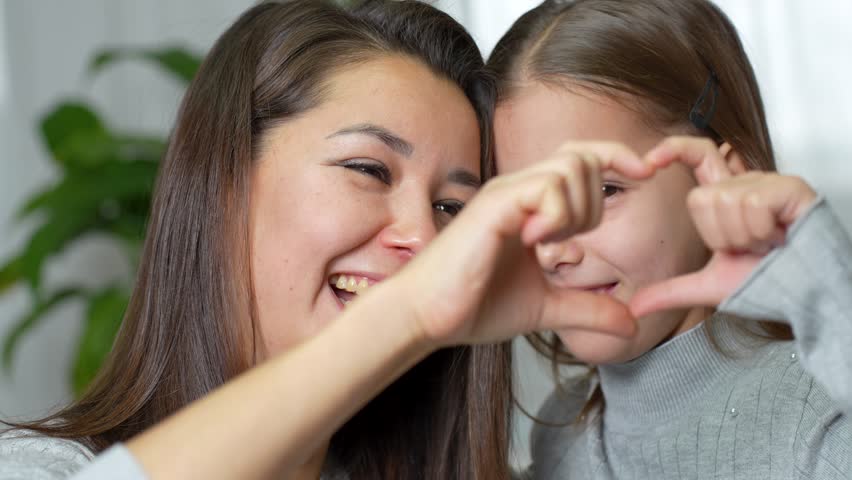 Happy mother and little daughter making heart with joined fingers, close-up. Young mother with her kid showing at camera love symbol express affection, feeling love, 4k slow motion
