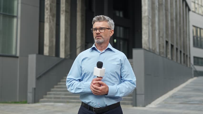 Attractive Caucasian male reporter crossing hands while holding microphone. Intelligent man getting ready to conducting interview on street. Enjoying working on television. Media coverage.