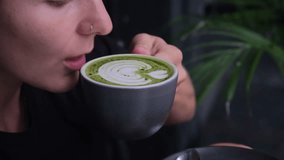 Beautiful woman drinking from mug of trendy matcha green drink with amazing latte art in hipster cafe. Organic green mast is filled with healing powers. Ideal morning concept with green coffee. - Powered by Shutterstock - Get 15% off with code: PIKWIZARD15