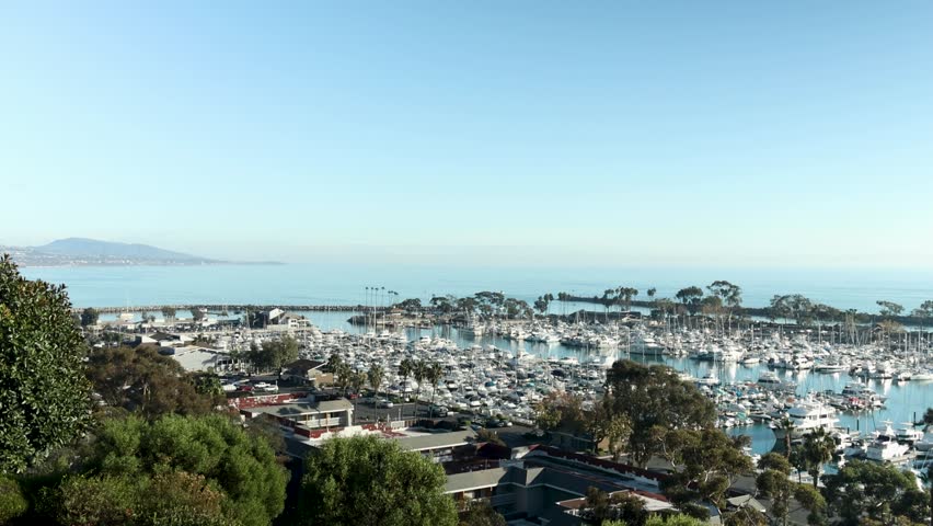 panning footage of the boats and yachts docked in the Dana Point Harbor with vast blue ocean water and lush green trees at Dana Point Bluff Top Trail in Dana Point California USA Royalty-Free Stock Footage #1112065973