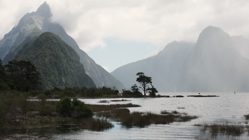 Panorama of Milford Sound, majestic cloud-shrouded peaks rise from the depths of a mirror-like fiord
