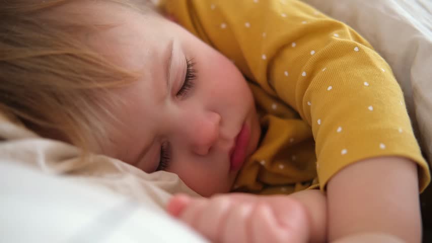 Peaceful adorable baby sleeping on a bed at home. Slumbering little child. Two year old girl sleeps peaceful at domestic room interior background. Serene dream. Cute face close up. Deep kid slumber | Shutterstock HD Video #1112067675