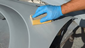 Manual cleaning of a car part for further painting. In the video, a hand in a blue glove with a special roller and grater cleans and smoothes the surface for painting.