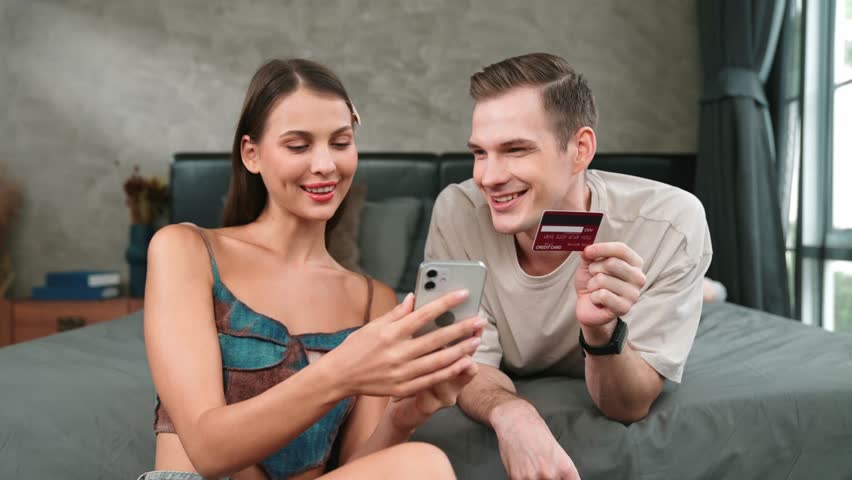 Young couple sit in the home bedroom using online payment app and digital wallet on smartphone to pay with credit card. E commerce shopping and modern purchasing via mobile internet. Adit Royalty-Free Stock Footage #1112071175