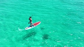 Aerial drone video of man in a paddle surf board known as Sup surfing in turquoise clear waters