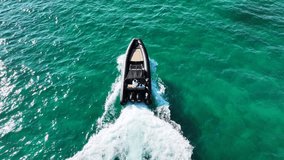 Aerial drone tracking video of inflatable rib speed boat cruising in high speed in deep emerald sea