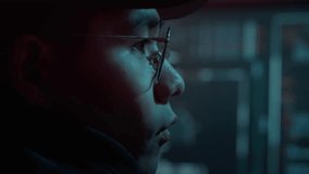 Side view and close up of serious asian network security analyst looking on modern displays with important work information. Virtual thief wearing black cap and glasses cap focused on cyber crime. - Powered by Shutterstock - Get 15% off with code: PIKWIZARD15