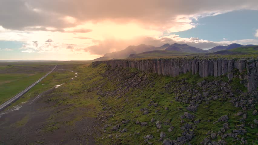 Epic Long Drone Tour Gerduberg Cliffs Iceland Sunset Landscape Row of Hexagonal Basalt Columns. Near Road Towards Setting Sun Over Wall of Columns. 4K High Quality Color Corrected. Royalty-Free Stock Footage #1112083407