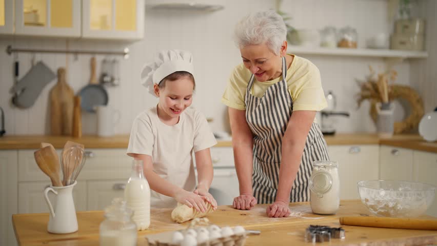 Granny teaching granddaughter to cook. Family senior grandmother child girl bake cookies laugh together on kitchen at home. Child throws dough on table. Cooking bakery preparing food bake concept. | Shutterstock HD Video #1112086925
