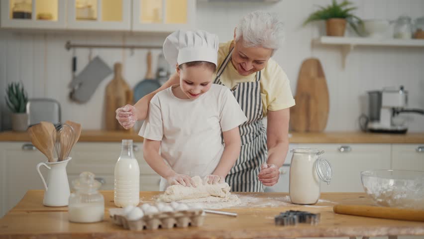 Granny granddaughter cooking at home. Family senior grandmother teaching child girl kneading dough on table, baking together on kitchen. Cooking culinary cuisine bakery preparing food bake concept. | Shutterstock HD Video #1112086929