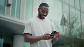 Contented man reading message good news in smartphone typing answer chatting online in messenger social media. Smile african american guy looking at mobile phone screen stand on city street outdoors. - Powered by Shutterstock - Get 15% off with code: PIKWIZARD15