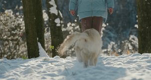Woman running in the snow with her dog, having a good time on a walk in the winter forest