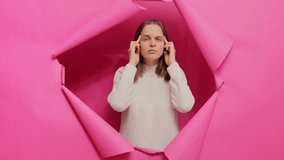 Tired unhealthy ill brown haired woman wearing sweater posing through hole of pink paper wall massaging painful temples suffering terrible headache grimacing. - Powered by Shutterstock - Get 15% off with code: PIKWIZARD15