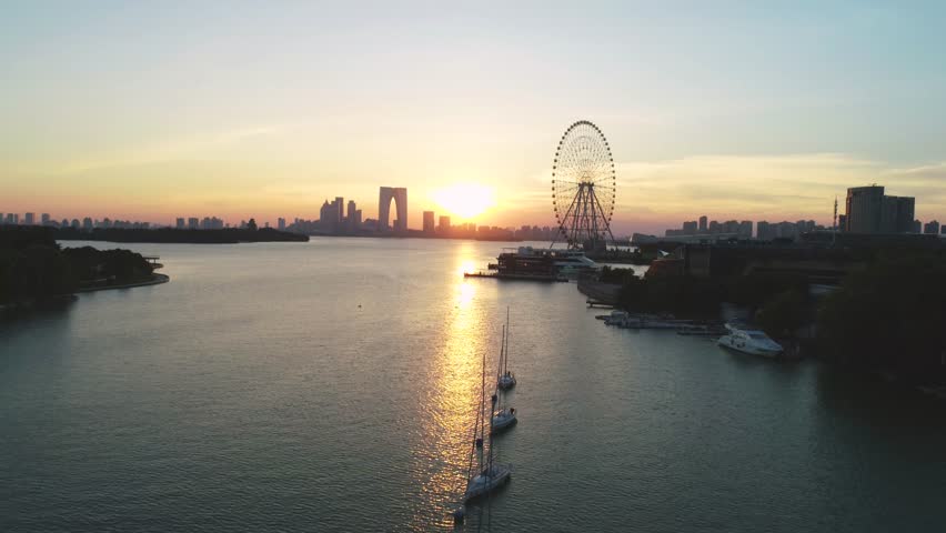 Aerial cityscape of a ferris wheel, boats and skyline in the sunset on Jingji lake, Suzhou, China. Camera moves forward