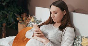 Happy young smiley pregnant woman holding a cellphone before putting it down to speak softly to her unborn baby, creating an intimate moment of love and connection.