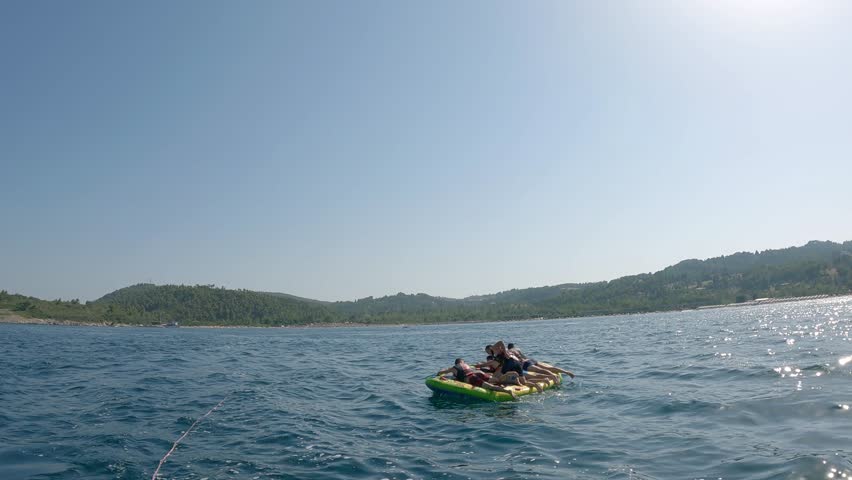 Excited friends, family having fun tubing on water rubber ring ride pulled by high speed water yacht speedboat during summer vacation