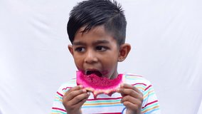 An Asian child is eating a slice of pink Dragon fruit on an isolated white background. A Kid holding or eating fresh Dragon fruit. Fresh fruit-eating and enjoying concept 4k video.