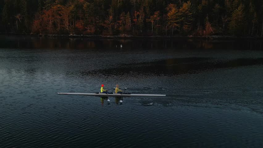 White rowing boat in motion with two women, aerial view. Drone shot of a rowing race, early morning training in an ocean bay. Aerial view of rowing. Rowing on the water from a bird's eye view.