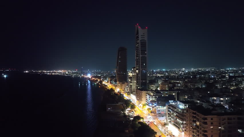 Aerial view of the night cityscape of Limassol, Cyprus. Lights of the city with the light of headlights of cars and streets on the shore of the Mediterranean Sea. High quality 4k footage