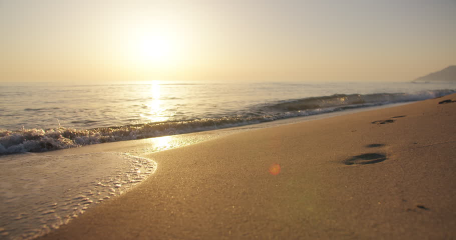 Waves of sea rolling in sunshine to the sandy beach. Close-up shot of calming foamy water