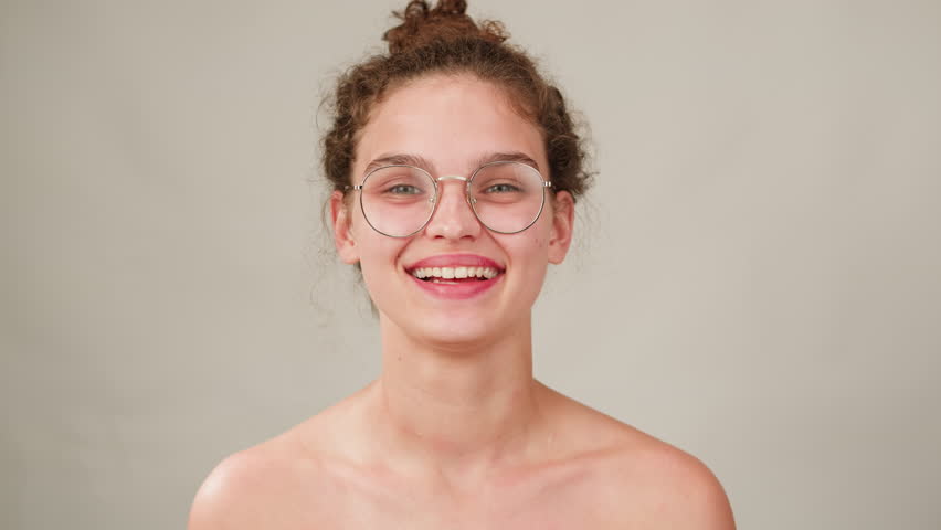 Young attractive brunette woman with curly hair in a bun wearing pink glasess close-up, white background. Portrait