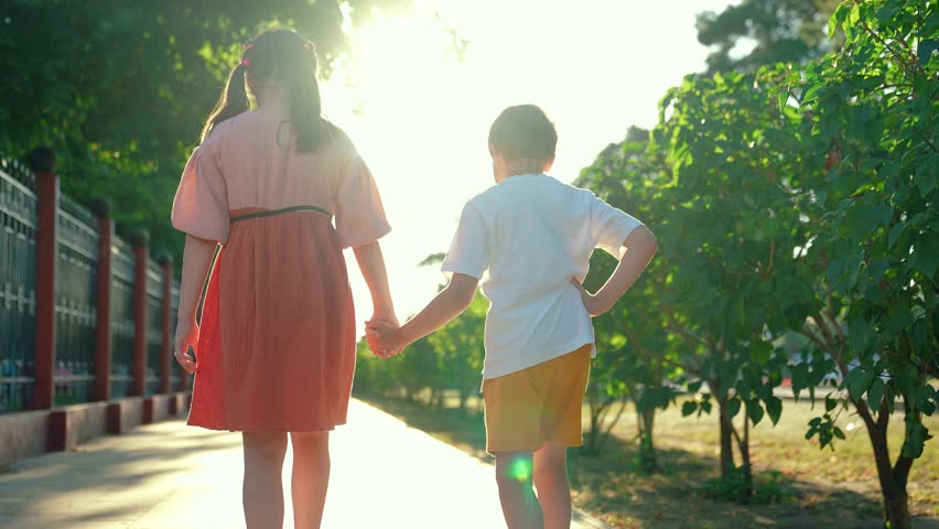 Happy children boy, girl, walk along city street, holding hands. Brother sister walking together. Happy children friends outdoors. Kids friendship. Children walk together in city park hand in hand.