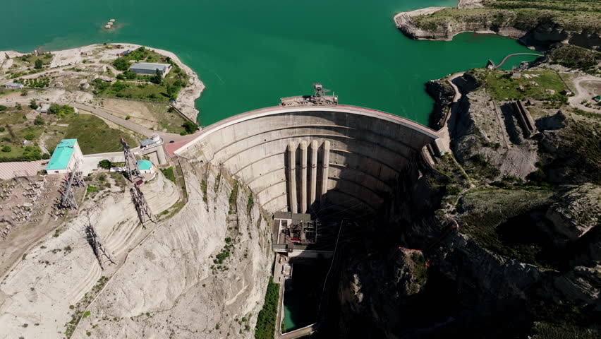 Amidst the serene summer landscape, a grand dam stands tall, its reflective waters encircled by rugged mountains and dramatic cliffs, beckoning travelers to embark on an outdoor adventure