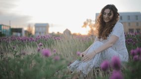 Beautiful young caucasian woman woman sit in the field with cute violet flowers.Portrait video.Close up.
