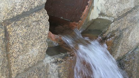 closeup Large underground drainage culvert dumping water under a city street with fast running water, actual audio