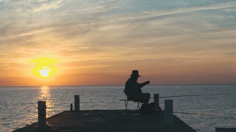 Man fishing on pier at the beautiful sunrise, silhouette