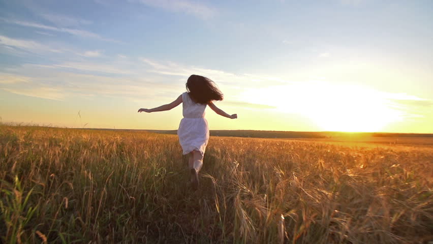 A Young Girl Happily Running Through A Field Of Golden Wheat At Sunset Slow Motion Rear View