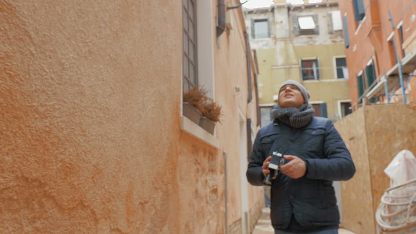 Steadicam shot of young man with vintage handheld camera capturing on video buildings of old city.