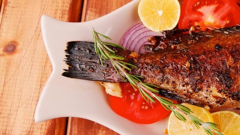 healthy lunch : whole fried sea sunfish on wooden table with lemons peppers and tomatoes and rosemary twig 1920x1080 intro motion slow hidef hd